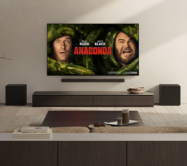 Living room with wall-mounted TV displaying the film poster for Anaconda, starring Paul Rudd and Jack Black, as part of the Sony Pictures Core promotion. A soundbar and speakers are arranged beneath the screen.