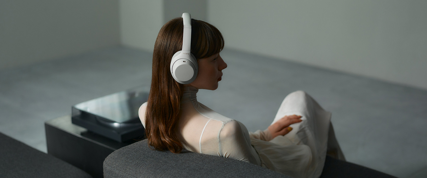 אישה מאזינה לאוזניות Sony WH-1000XM4C בבית