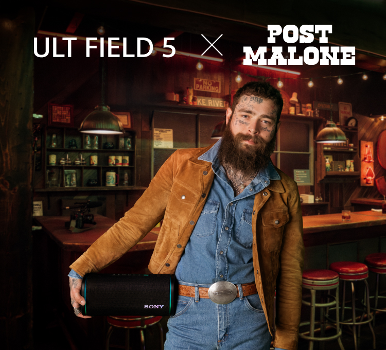 Post Malone in denim and a brown jacket holds a Sony speaker in a cozy bar setting. "ULT FIELD 5 x POST MALONE" text is visible on the left. Warm, inviting atmosphere.